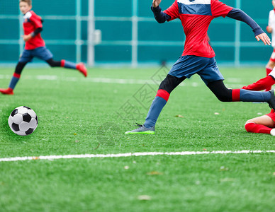 穿着红色和白色运动服的男孩在绿草场上踢足球青少年足球比赛儿童体育比赛图片