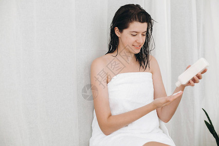 穿着白毛巾的年轻女子在家里的浴室里用手上涂着保湿霜图片