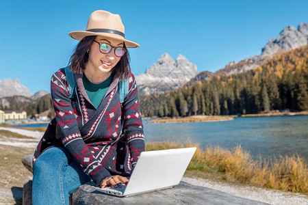 秋天在山湖背景笔记本电脑上工作的亚洲快乐妇女图片