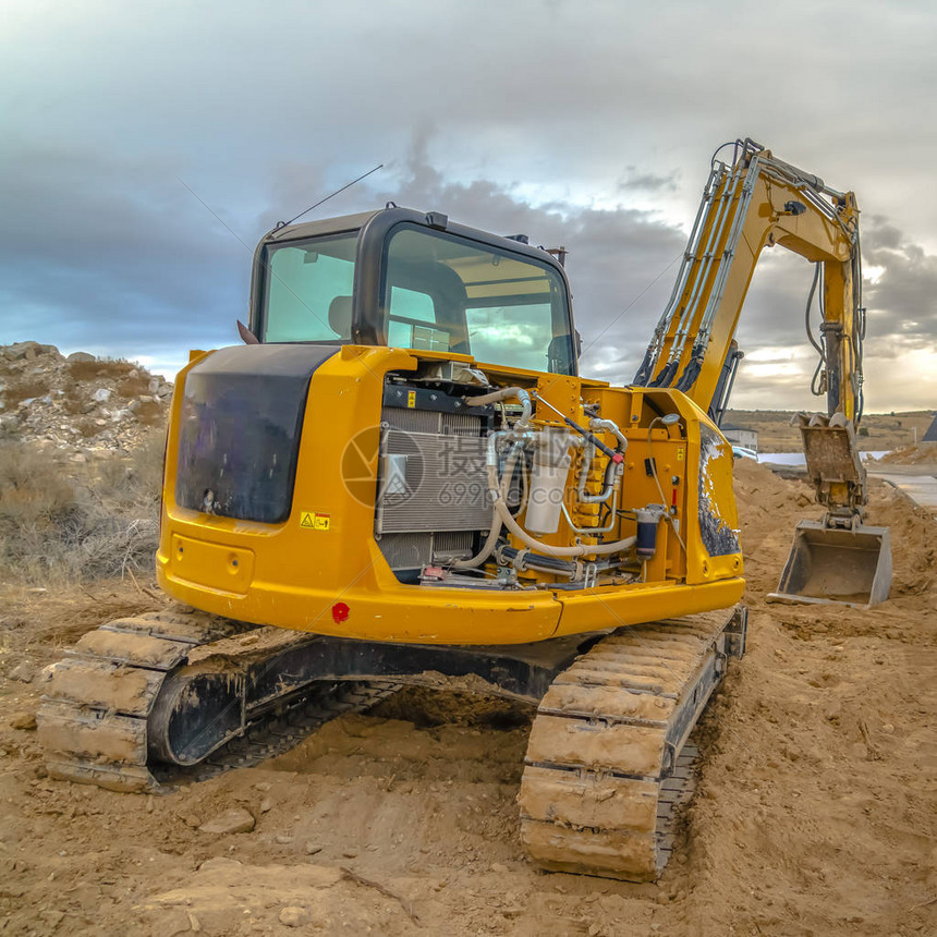 在多云的天空的泥土顶部的挖掘机挖掘机在犹他谷的一个建筑工地的一堆泥土上重型机械背后是一片乌图片