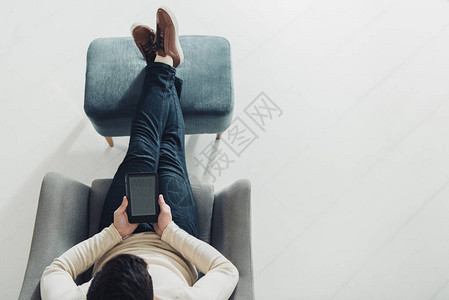 坐在家扶椅上时持有电子阅读器的图片