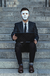 穿着面罩和笔记本电脑的商人看似直立图片