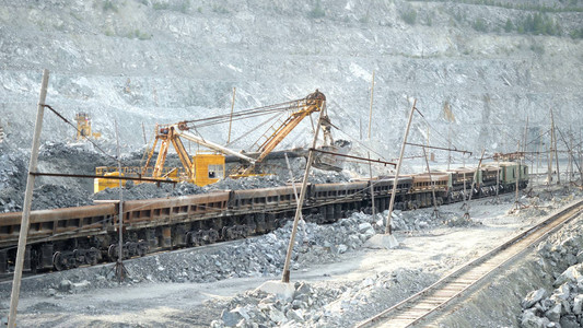 挖掘机和铁路与矿石挖掘机在露天矿坑的背景下装满了矿石轨道车采矿图片