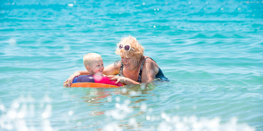 外婆和小孙子在海里游泳在充气的多彩圆圈里的孩图片