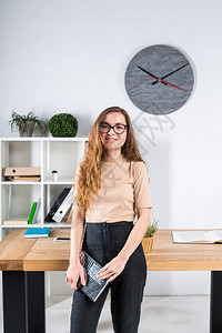 一位留着长发和戴眼镜的年轻白人女肖像站在办公桌附近的办公室内女大学生图片