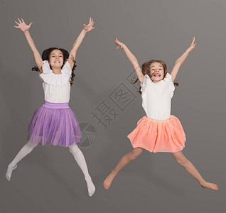 两个快乐的小女孩跳过灰色背景在空气中图片
