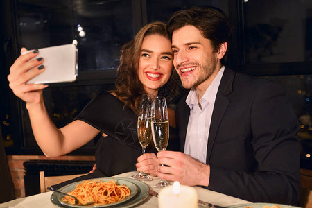 快乐的一对情侣在餐厅浪漫晚餐时用智能手机做自拍的肖像抓住欢图片