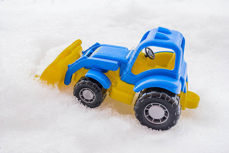 带前装载机的塑料蓝色和黄色玩具拖拉机在雪地里公用事业和除雪的概图片