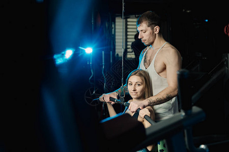 帅的运动男子帮助一个漂亮女孩在健身房的街区图片