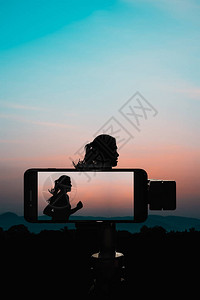 在三脚架上使用智能手机的游侠拍下一位有照片的年轻女子日出时跑来去带着图片