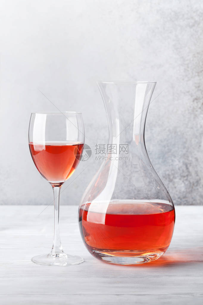 玻璃杯中的玫瑰酒和木桌上的滗酒器在石墙前图片