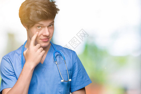在孤立的背景下穿着医疗制服的年轻医生指着眼睛看着你的手势图片