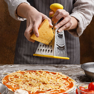 厨师在披萨上撒奶酪在餐厅厨房用刨丝器擦图片