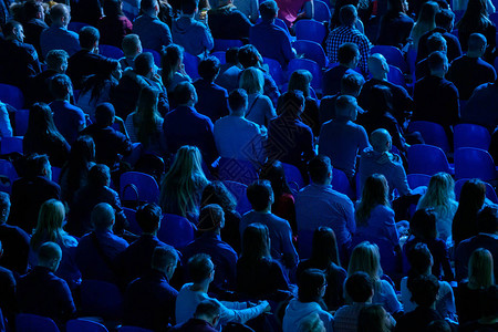 观众聆听商业会议演讲人背视蓝背景图片