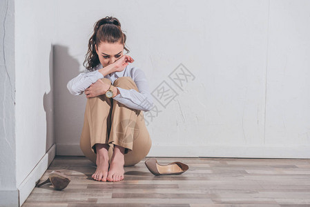 穿着白上衣和米色短裤的悲伤妇女坐在地板上图片