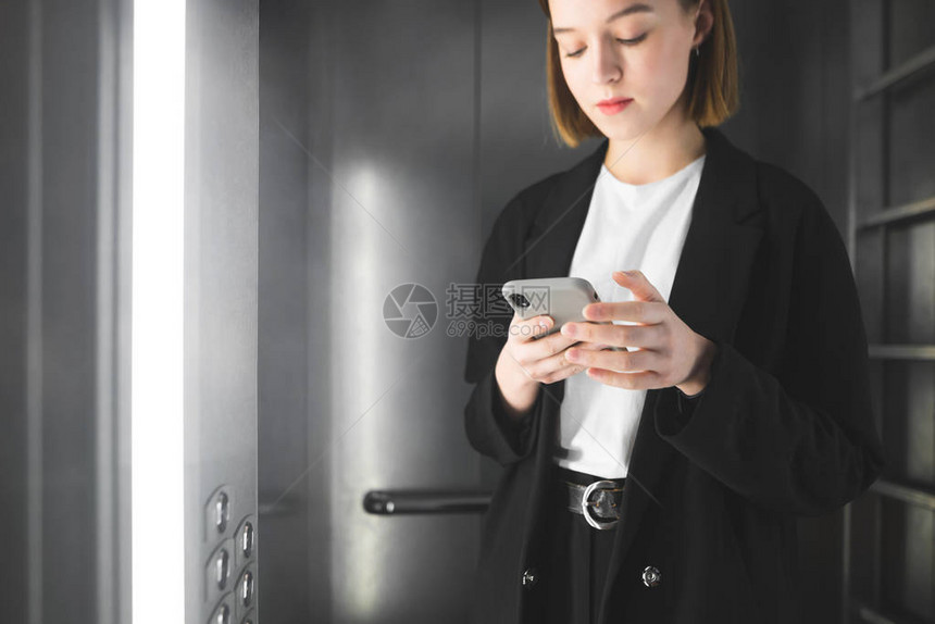 穿着智能西装的和平年轻女商人正在电梯里看着她的智能手机年轻的上班族正在电梯里用手机浏览I图片