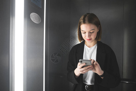 微笑的女上班族在电梯里使用智能手机年轻的女商人正在用她的智能手机上网图片