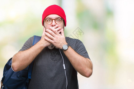 穿着红色羊毛帽和背包的年轻时髦男子在孤立的背景上被用手顶住图片