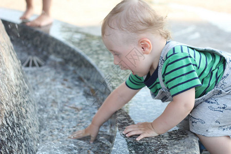 一个小男孩爬上喷泉的栏杆并触摸水图片