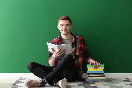 英俊的年轻人坐在彩色墙边看书图片