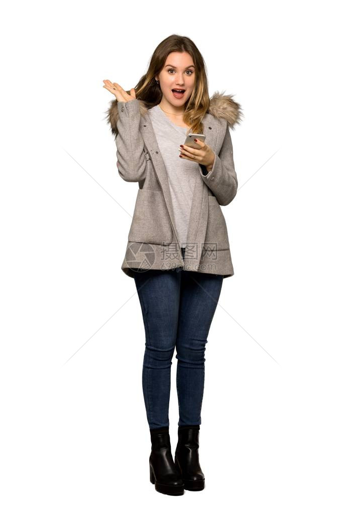 一个穿大衣的青少年女孩在用孤立白背景的手机发送讯息时图片