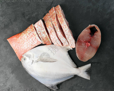 白色鲳鱼西班牙鲭鱼红鲷鱼清洗黑色大理石板背景上的去鳞图片