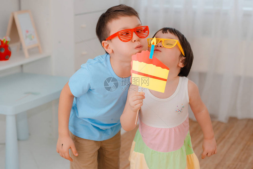 男孩和一个女孩用蜡烛玩道具纸蛋糕生日那天孩子们一起咬蛋糕的表演朋友们戴着有色眼镜玩得图片