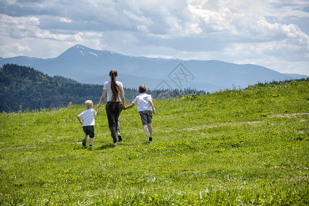 母亲和两个年幼儿子在绿地上奔跑图片