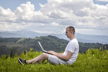 有笔记本电脑的人坐在山地背景的图片