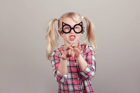 可爱的金发白种人学龄前女孩戴着滑稽的猫眼镜和玩耍表演做鬼脸的特写肖像图片