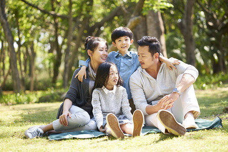有两个孩子的亚洲家庭与两个孩子一起玩乐坐在草地上聊天在图片