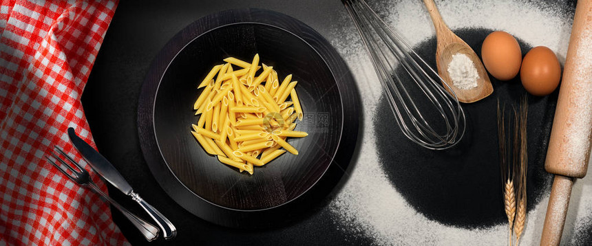 意大利面条在黑桌子上用木制厨房餐具面粉鸡蛋小麦和桌布的图片