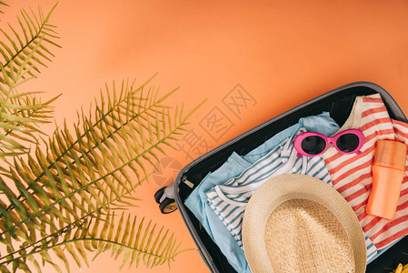 带有夏季附件和棕榈叶橙色背景防晒霜的手提箱顶部图片