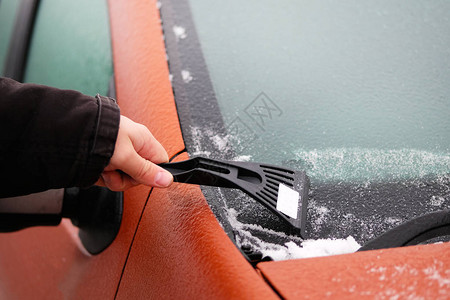 人手握着铲子用冰冷的挡风玻璃扫雪清理图片