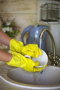 紧握着身戴黄色手套在厨房洗盘子的妇图片
