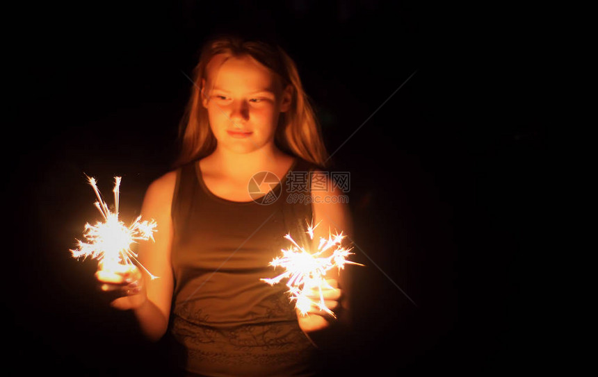 少女带着燃烧的火花在黑夜暗背景下握在她的手中图片