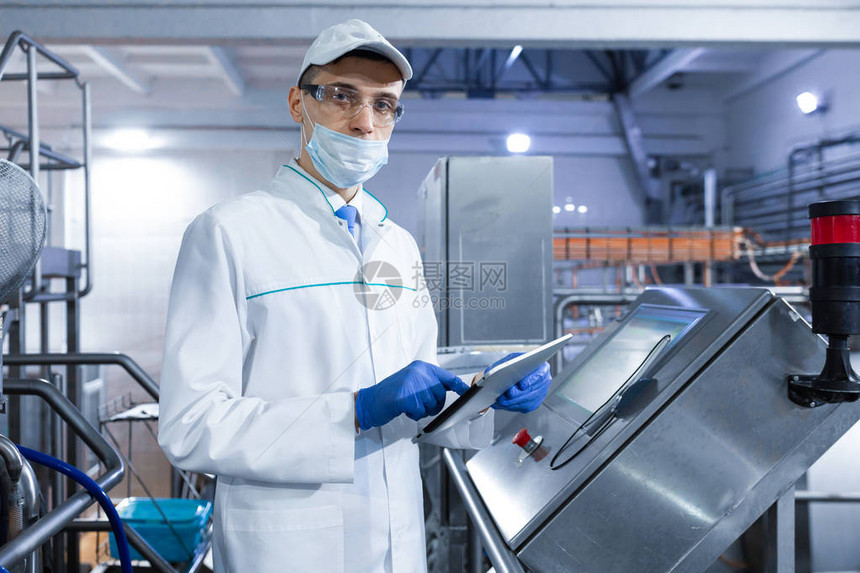 戴着帽子面具和白大衣的技术人员在生产车间里拿着数字平板电脑检查员删除了乳品厂的指标工程师图片