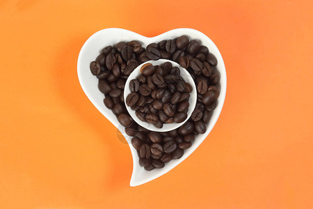 橙色背景上的咖啡豆白色陶瓷杯哈特爱形盘碗图片