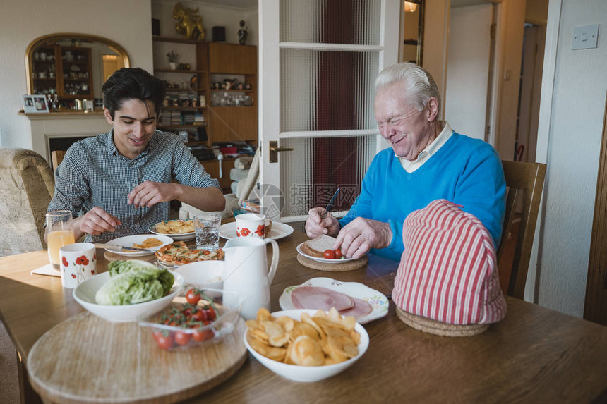老人和孙子在家吃午饭他们吃三明治披萨和薯片图片