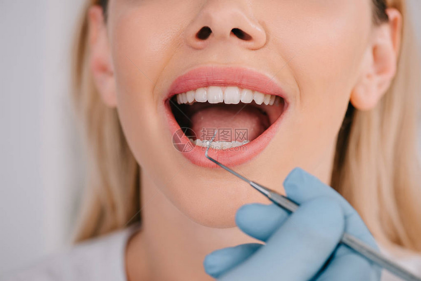 牙科医生用牙科探牙器检查年轻女牙图片