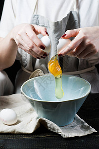 厨师在碗上打碎鸡蛋做饭侧观黑背景图片