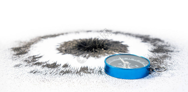 黑铁粉磁场下的强圆径向磁与白色背景上的蓝色罗盘科学课图片