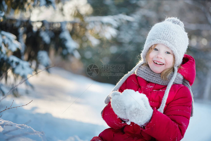穿红大衣的小女孩正坐在雪地里微笑图片
