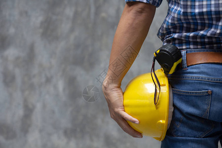 室外混凝土墙背景上手持黄色安全头盔的男建筑师工人图片