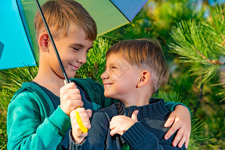 两兄弟站在明亮多色雨伞的拥抱下图片