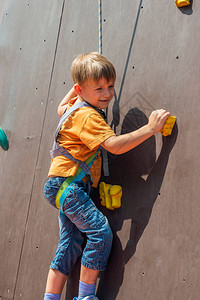 一个受惊的小男孩想用安全绳爬上人造岩石图片