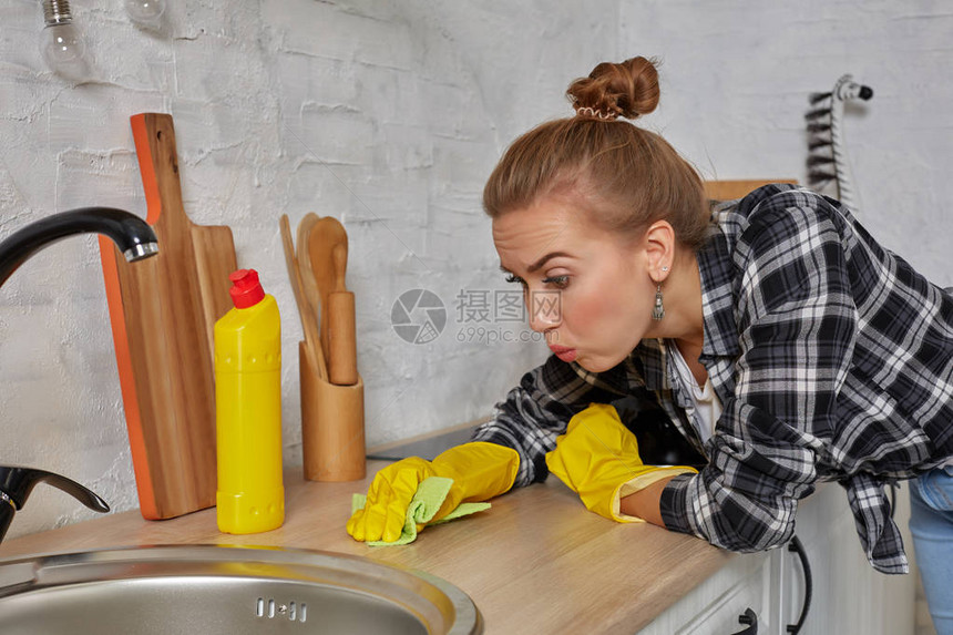 手部清洁年轻的家庭主妇在厨房里洗水槽戴着黄色清洁橡胶手套的年轻女子图片