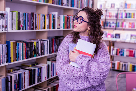 长头发有吸引力的女孩穿着超大毛衣背着一堆书参观公共图书馆时还图片