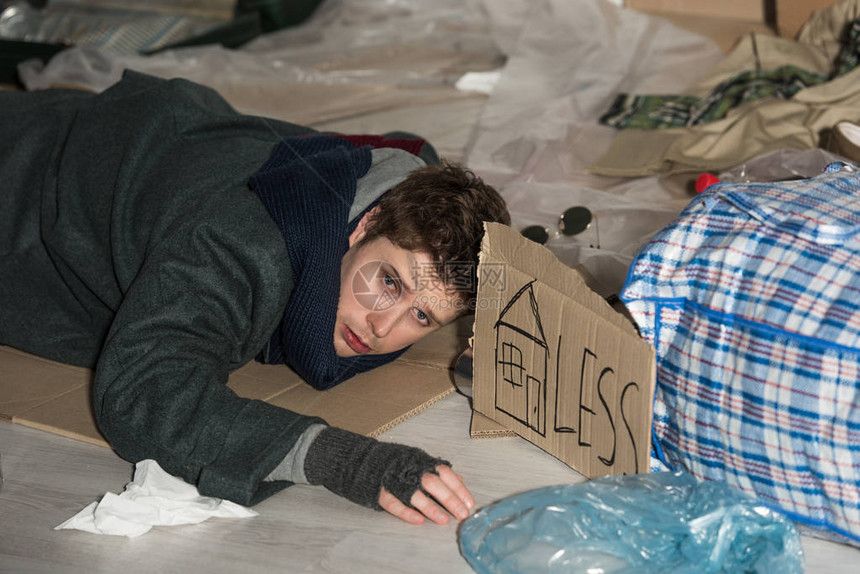躺在垃圾堆的纸板上有房屋符号和卡片无标记的无家可归的绝图片