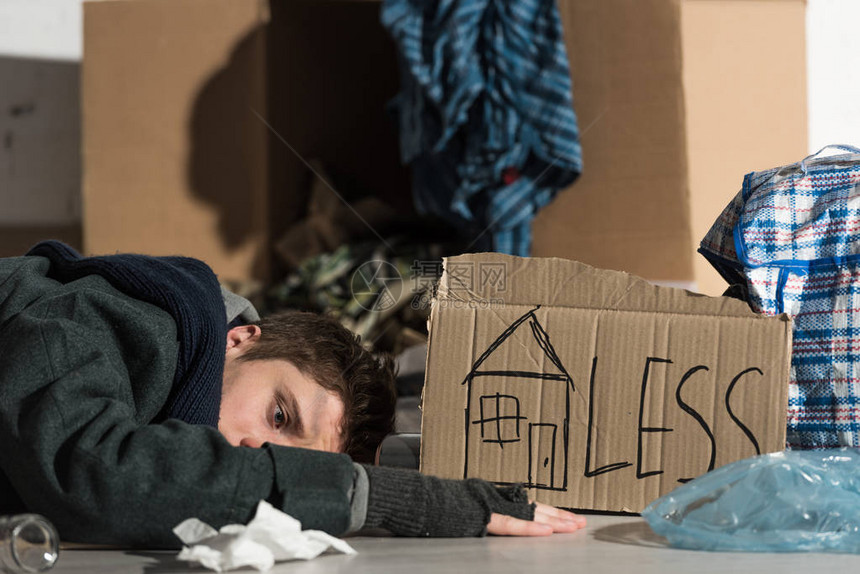 沮丧的无家可归者躺在垃圾场的纸板上图片